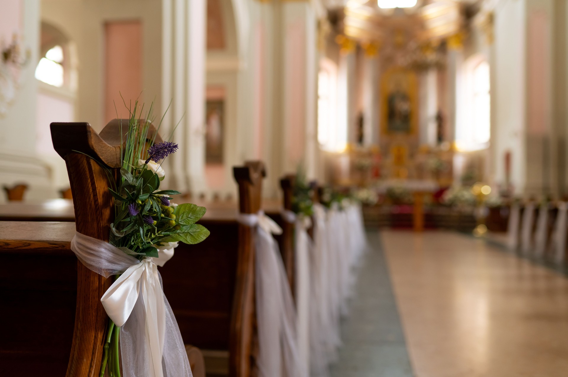 The benches in the church are beautifully decorated with white ribbons and flowers for the wedding ceremony
